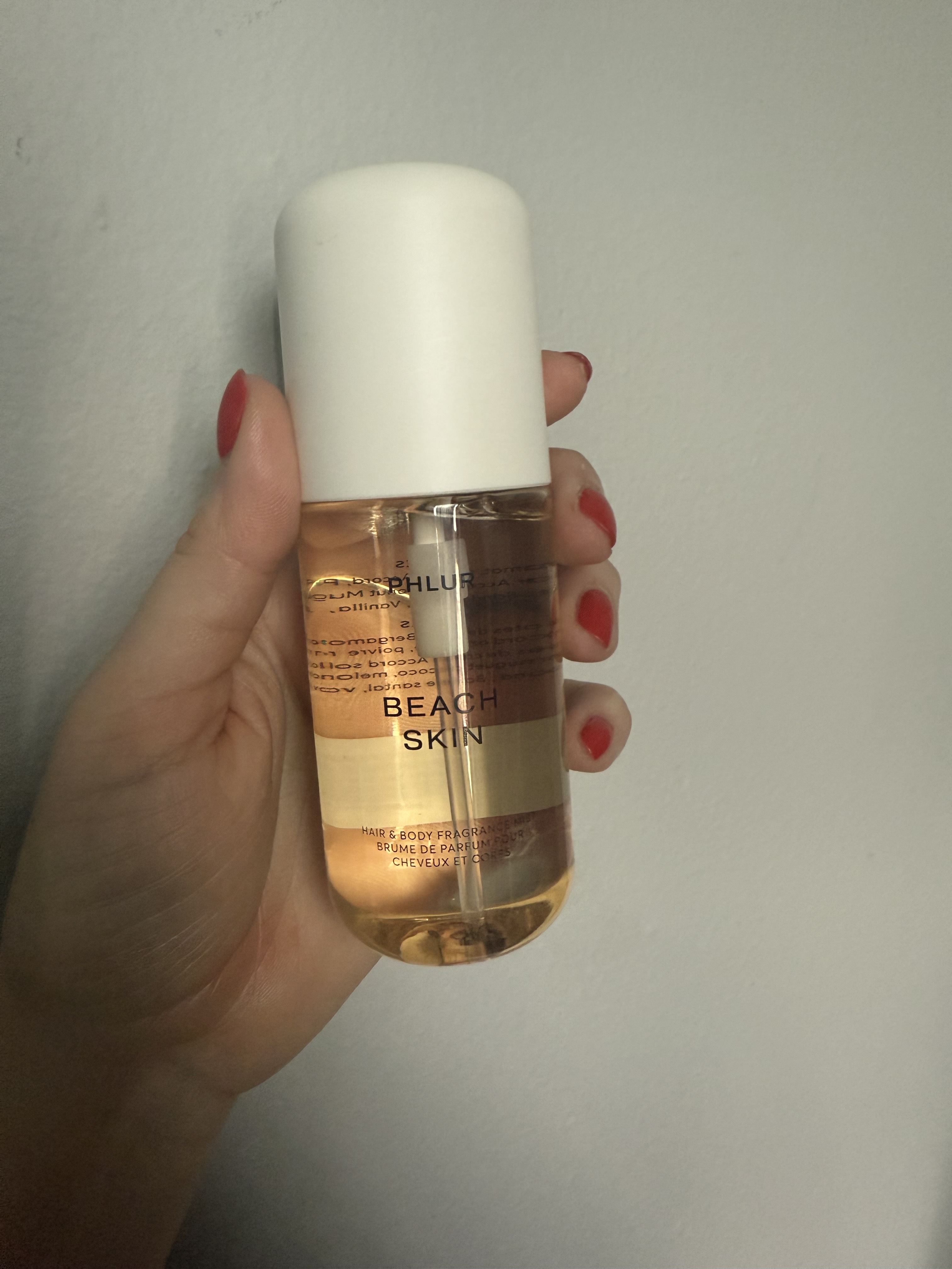 Hand holding up phlur Beach Skin Hair & Body Fragrance Mist against grey wall