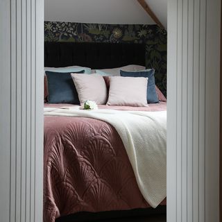 A glimpse of a bed with a pink velvet quilt and navy pillows through an open doorway