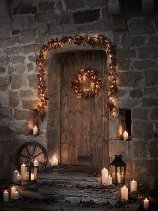 fall porch with lanterns, candles and LED lit wreath on door and garland