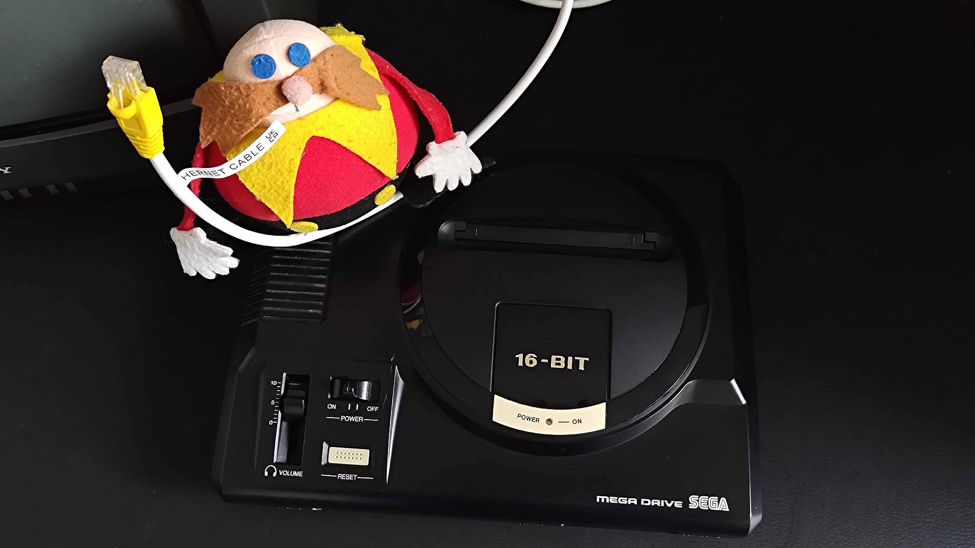 Sega Mega Drive model 1 console next to '90s Dr Robotnik plush holding ethernet cable.