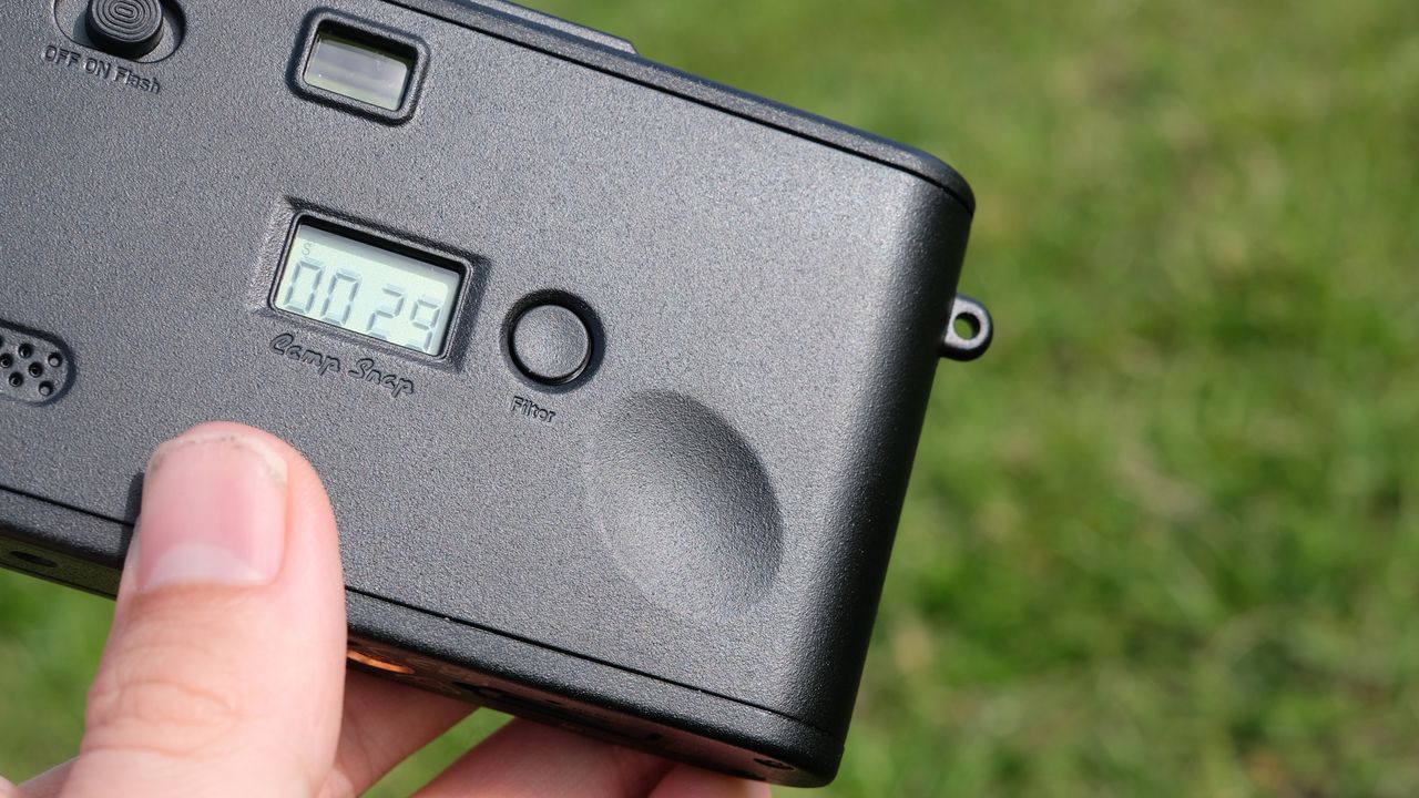 Photograph of man's hand holding Camp Snap 2 digital camera, in yellow colorway, close up of thumb groove on rear