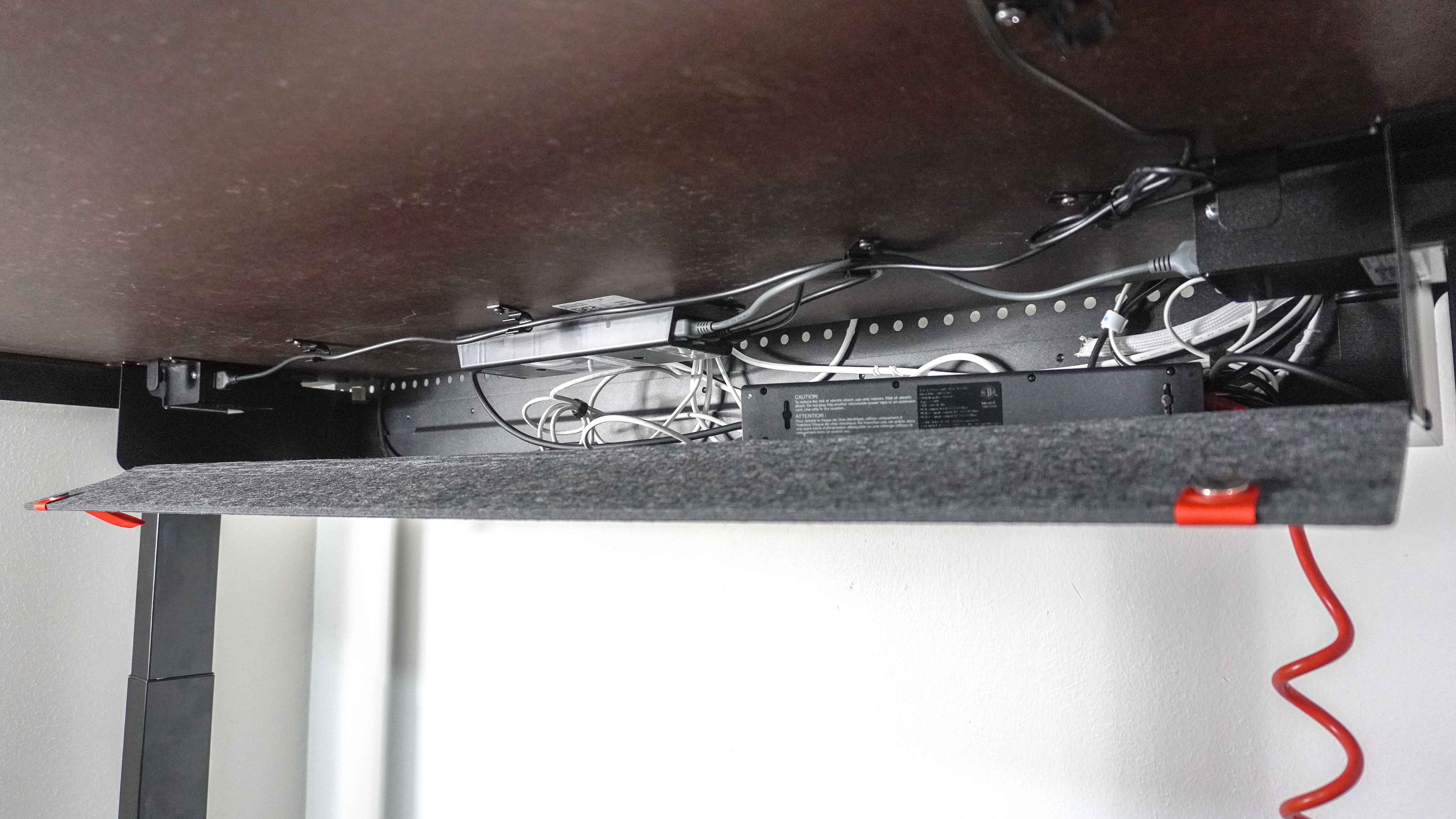 An angled shot showing the the cable trough under the Herman Miller Coyl Gaming Desk filled with power adapters and a surge protector