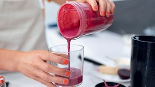 A personal blender tipping a berry smoothie into a glass