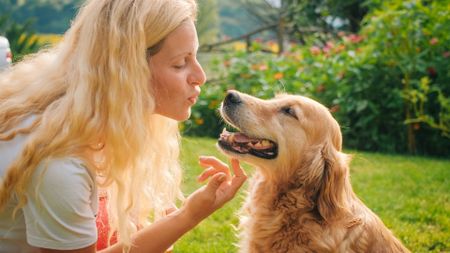 A woman with long blonde hair kisses her blonde golden retriever