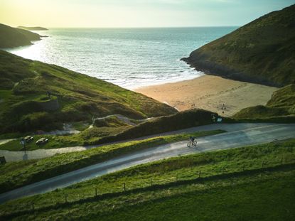 A cyclist riding next to the Welsh coast as the sun sets in the background