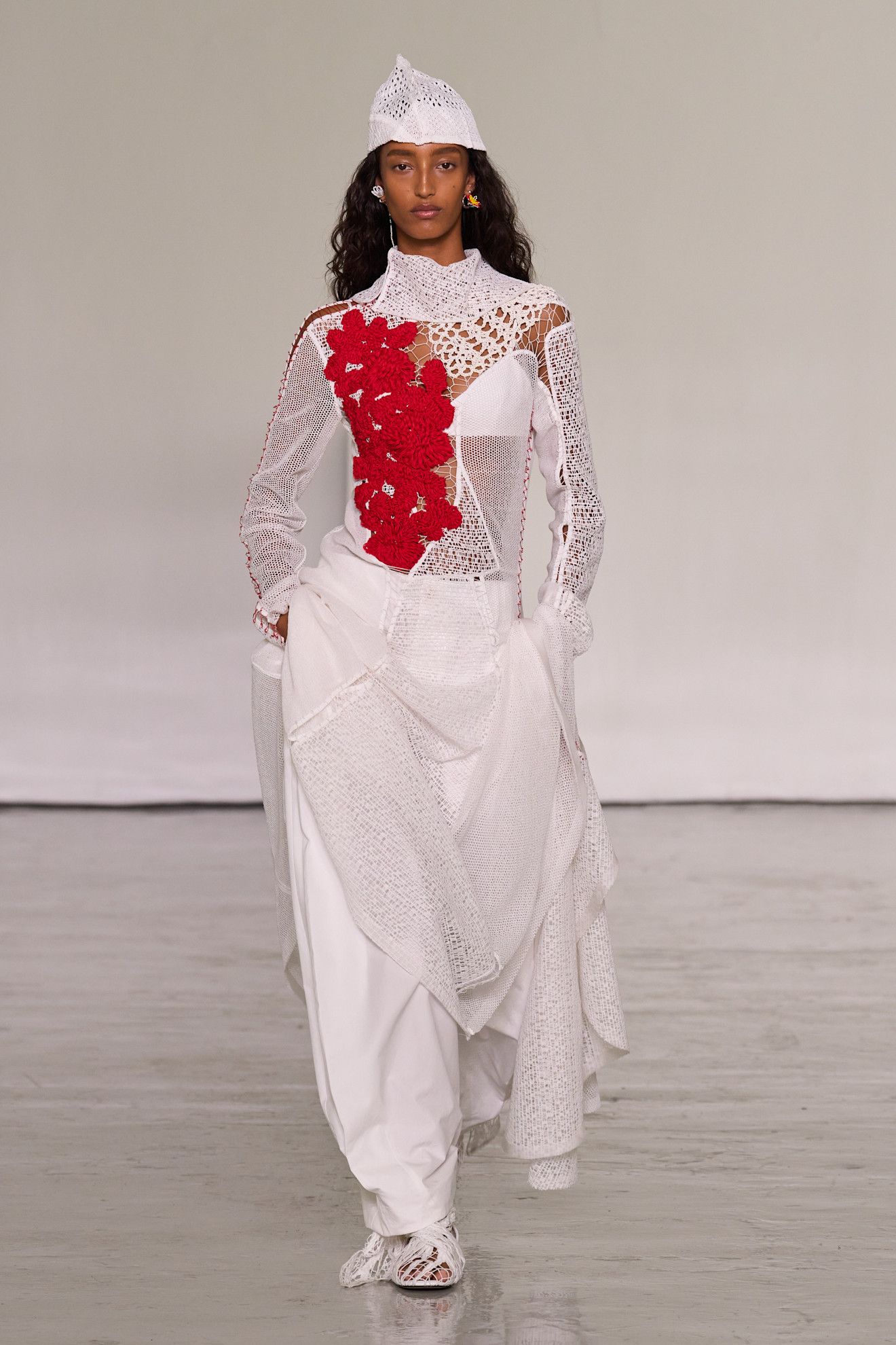 A model walking in the spring/summer 2027 Bottega Veneta show during Milan Fashion Week wearing a crochet hat and top with white poplin pants.