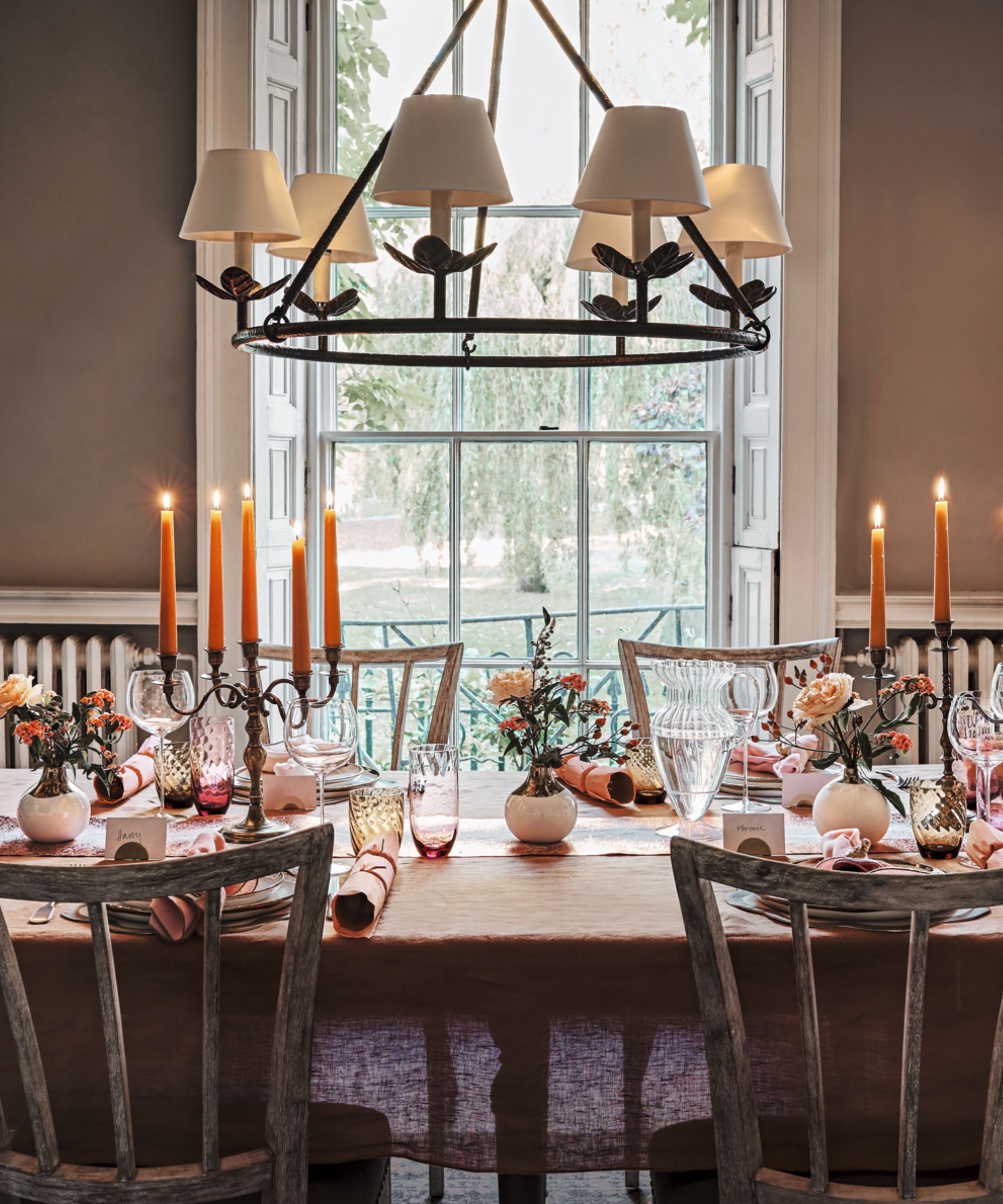 Dining table with candelabras, orange and pink glassware and bud vases of flowers
