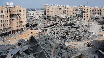 Displaced Palestinians walk amid the rubble of houses destroyed by Israeli bombardment in Hamad area,