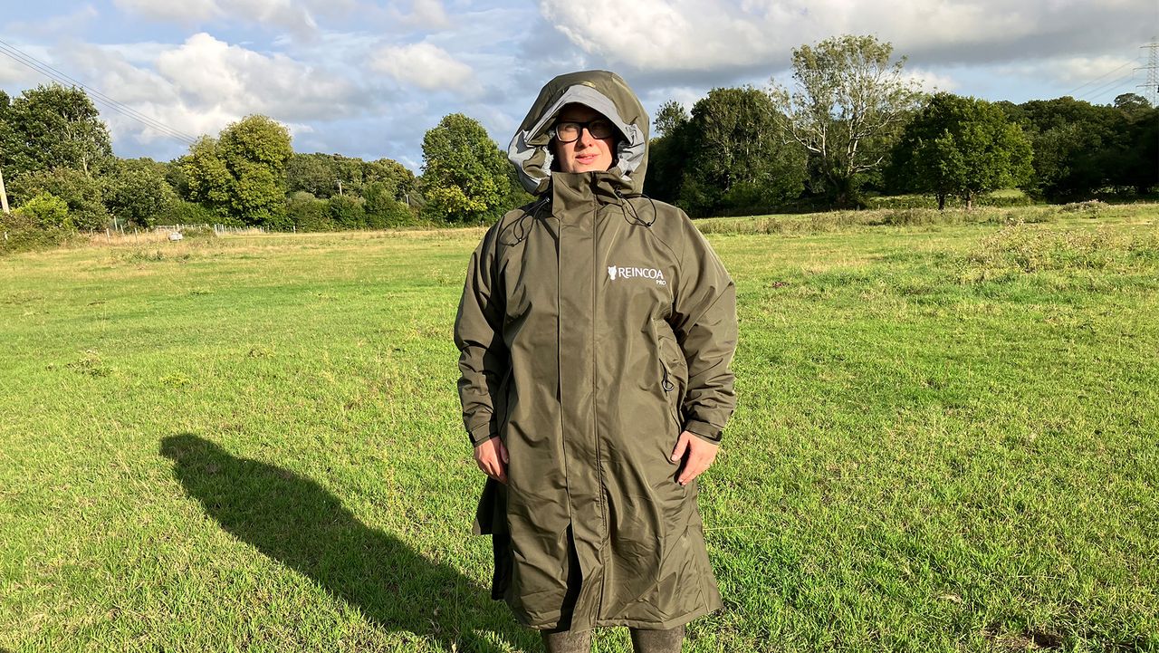 Lady wears Reincoat Pro in a field with hood up, viewed from the front