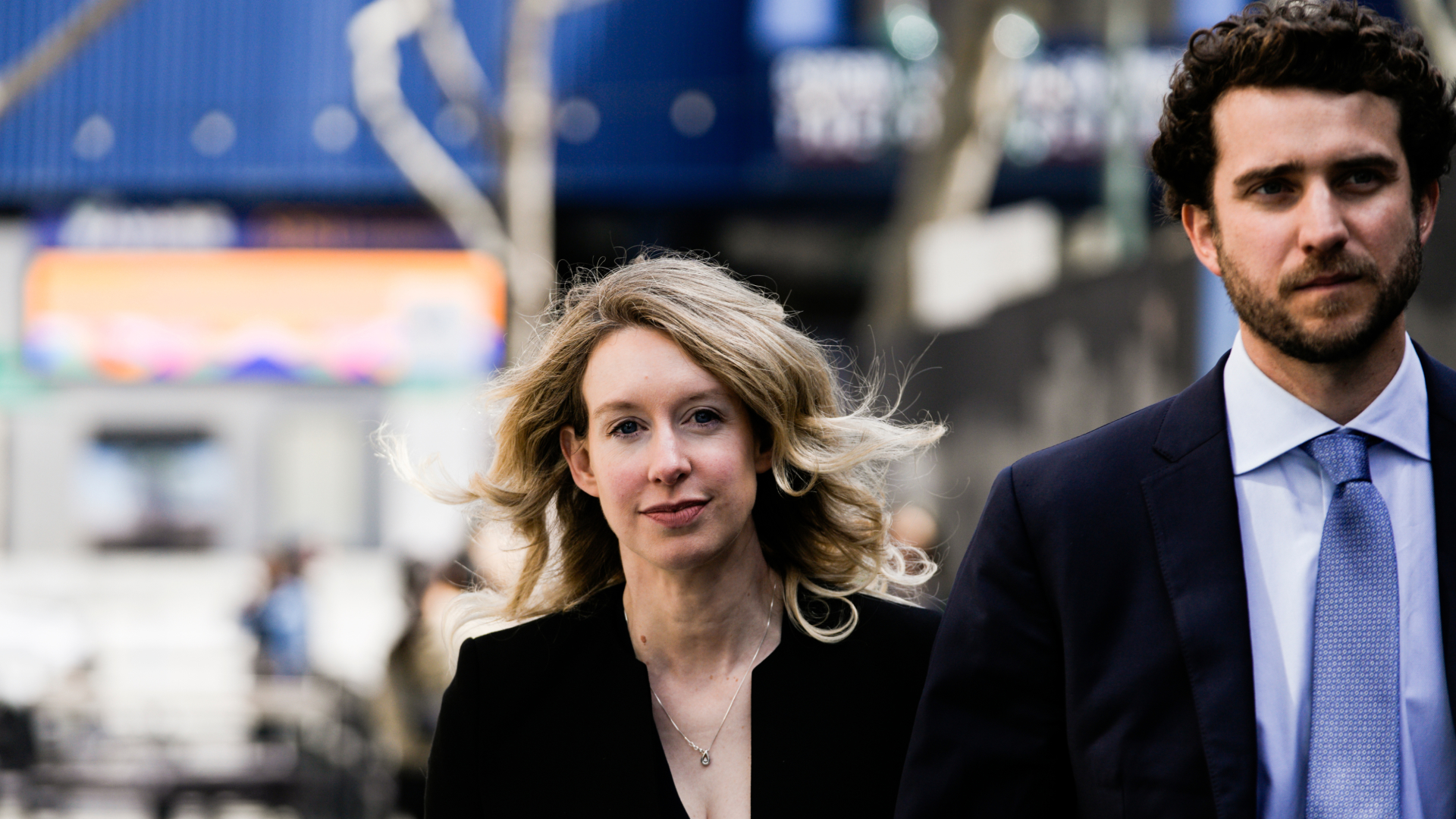 Elizabeth Holmes and Billy Evans walk together outdoors, with Holmes looking toward the camera.