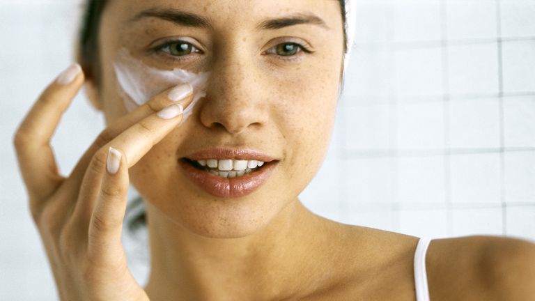 Woman applying moisturizer beneath eye 