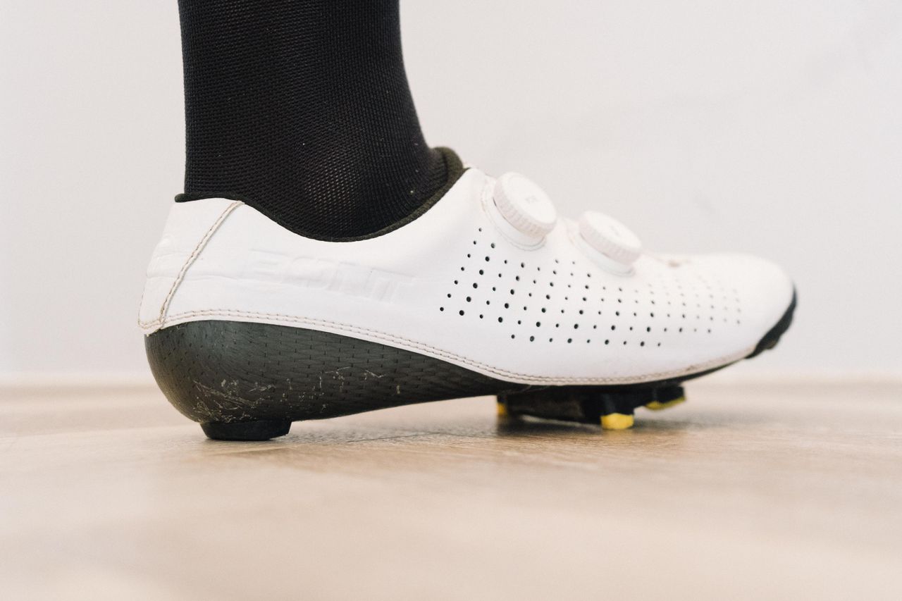 A close up of a white cycling shoe with a black socked foot in it