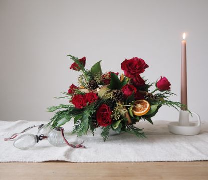 Christmas table centerpiece with foliage, red roses, dried fruit, baubles on table and candlestick