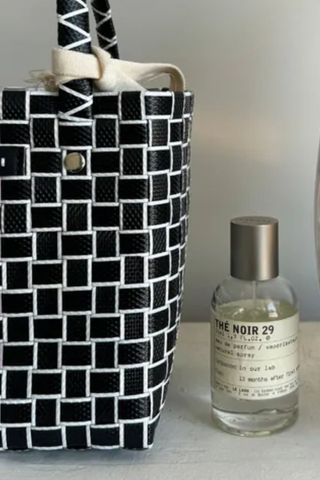 a close up shot of a bottle of Le Labo The Noir 29 next to a handbag