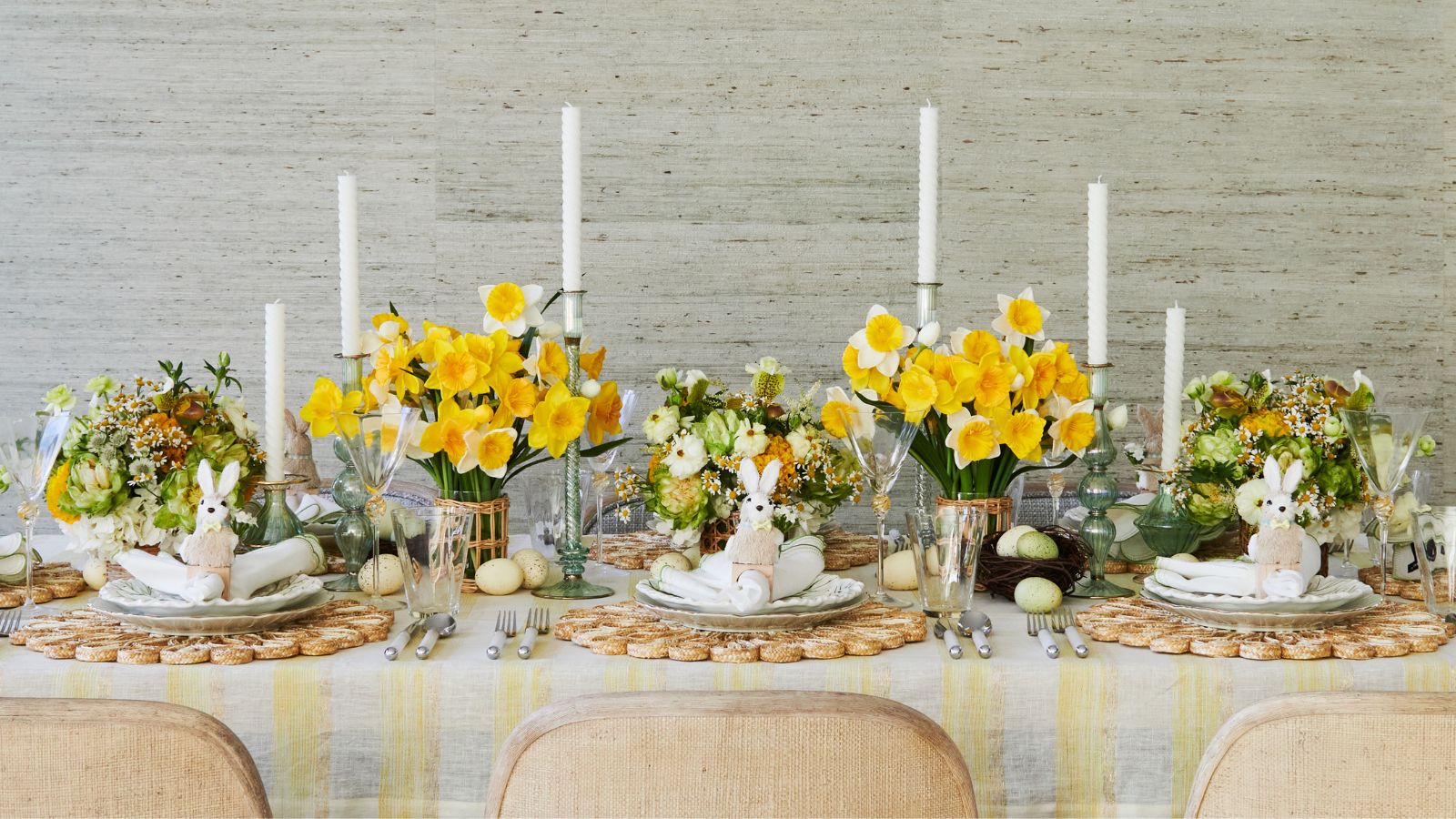 Spring tablescape featuring vases of yellow daffodils, a yellow stripe tablecloth, rattan placemats and easter bunny napkin rings