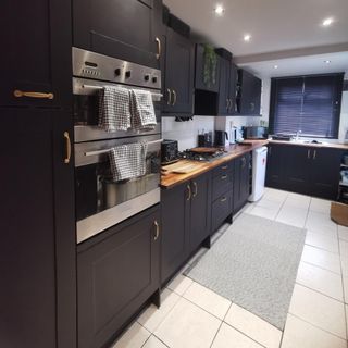 black kitchen cabinetry with neutral floor tiles and patterned rug