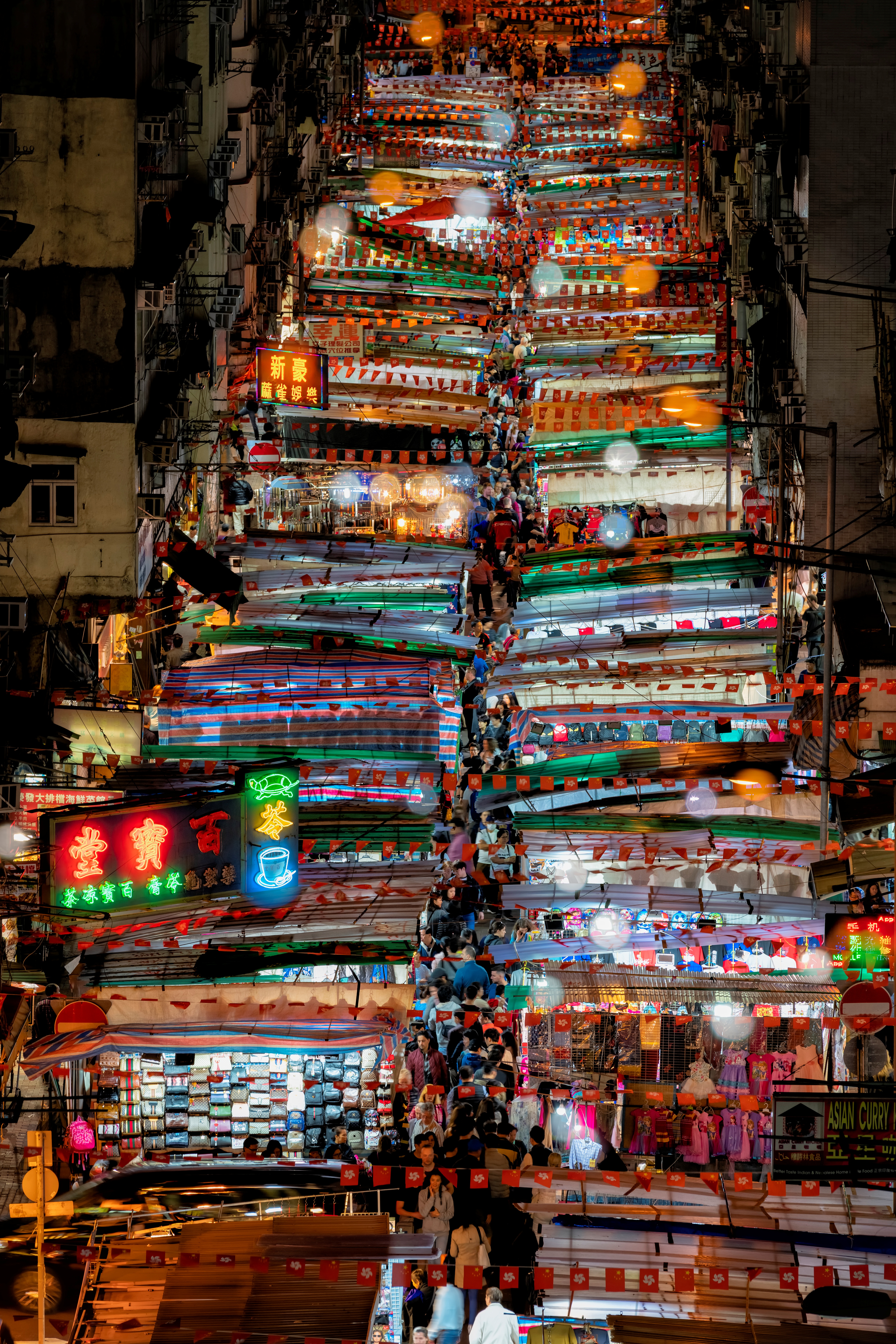 A nocturnal view of a colorful, neon-lit market crowded with people and captured from above.