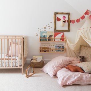 a child's bedroom with a cot, floral bed linen, two wall-hung book display shelves and a comfy reading nook with cushions and a canopy