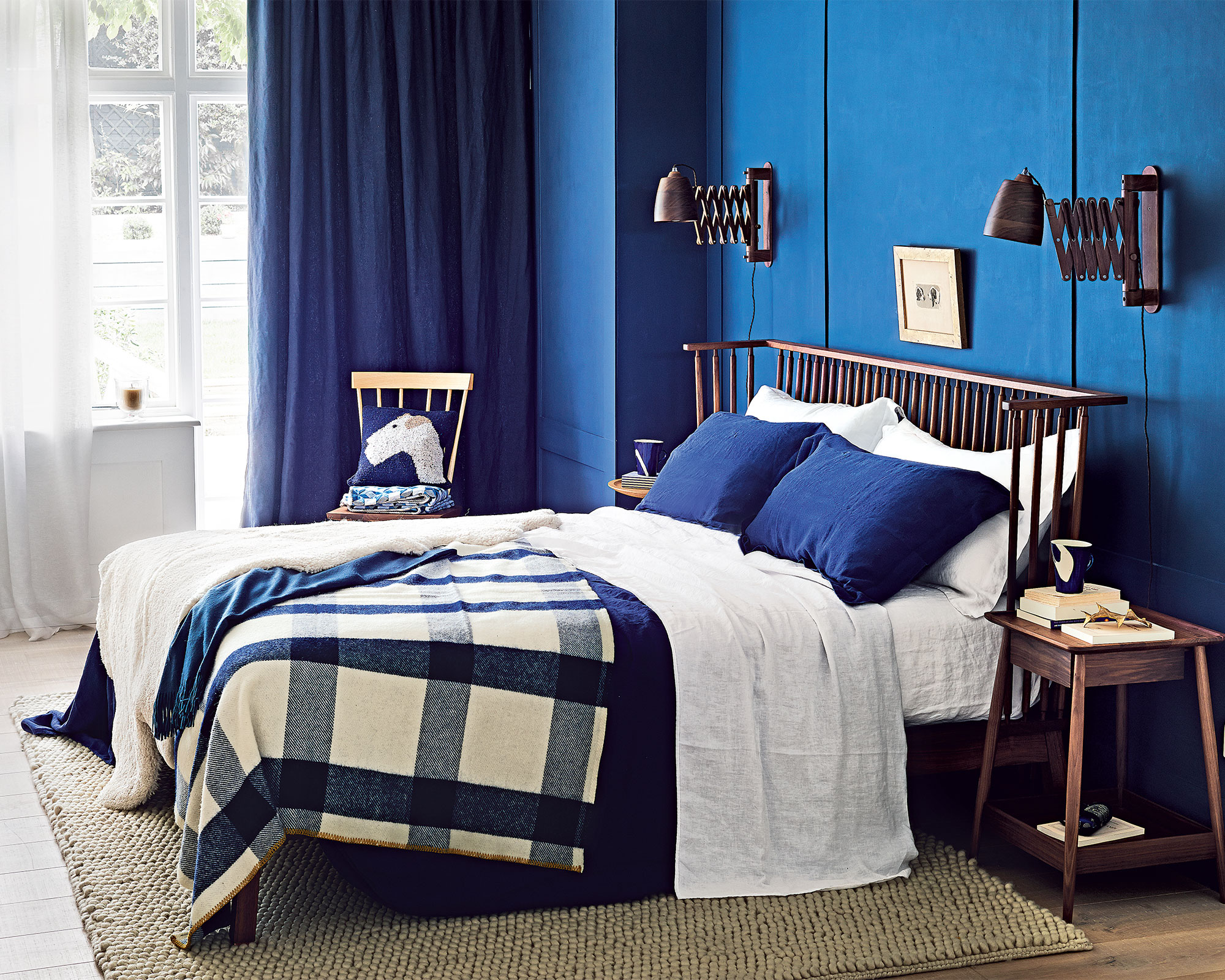 An example of bedroom wall lighting ideas in a dark blue scheme with large window and bed with check throw.