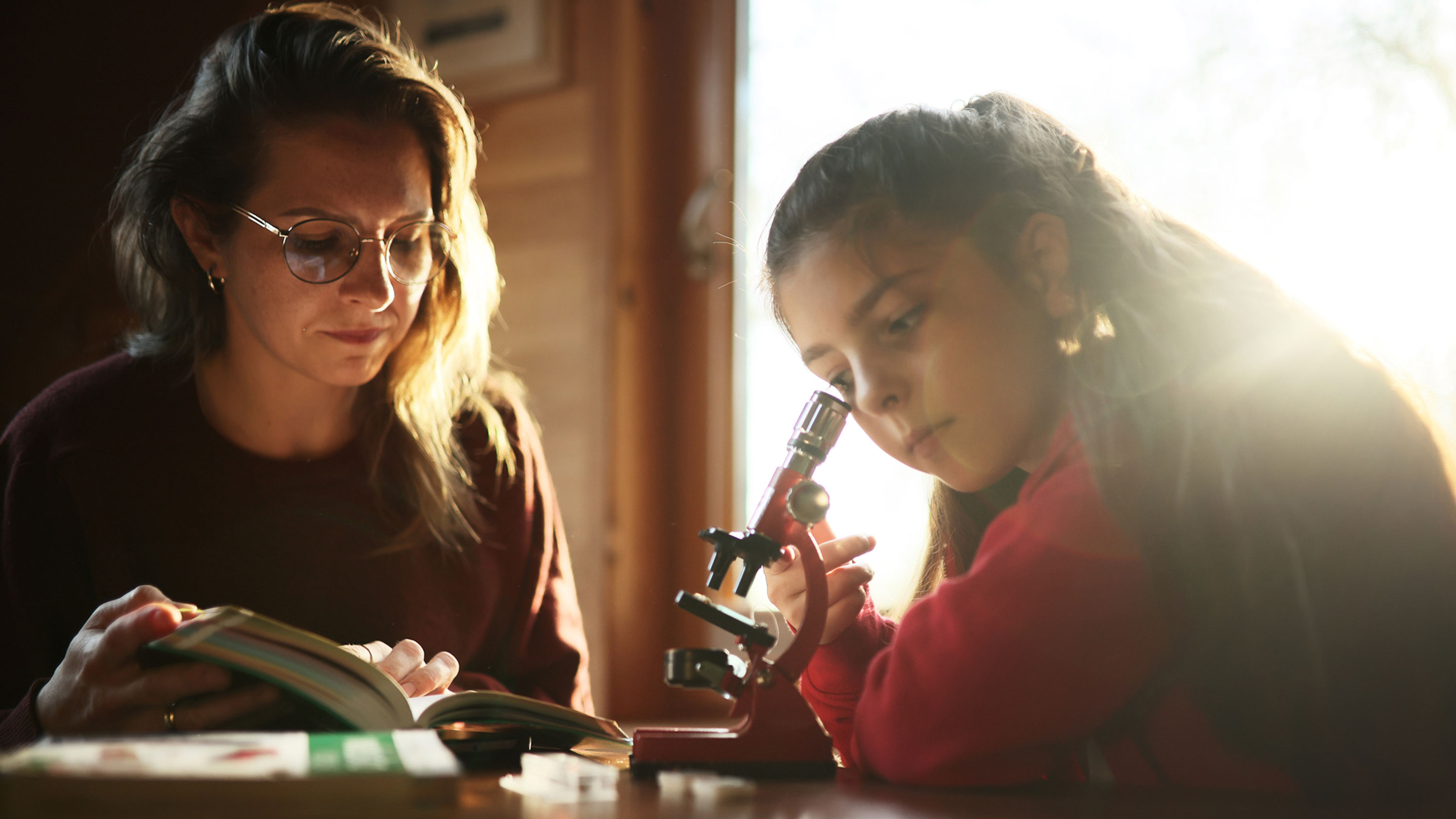 A woman and a young girl use a microscope to observe something small