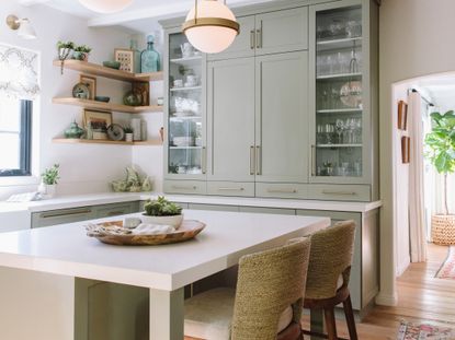 A kitchen with sage green cabinetry, open shelving, and island