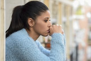 A woman sits, looking worried.