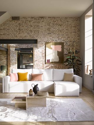 apartment with exposed brick wall, white sectional couch, herringbone floor, rug, coffee table, artwork