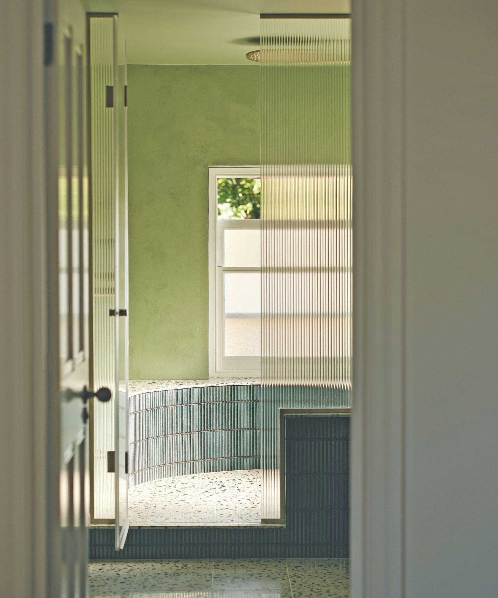 Green bathroom with raised shower area with tile and ribbed glass