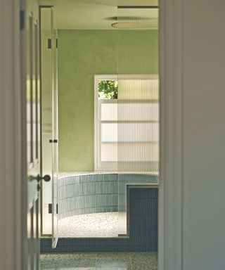 Green bathroom with raised shower area with tile and ribbed glass