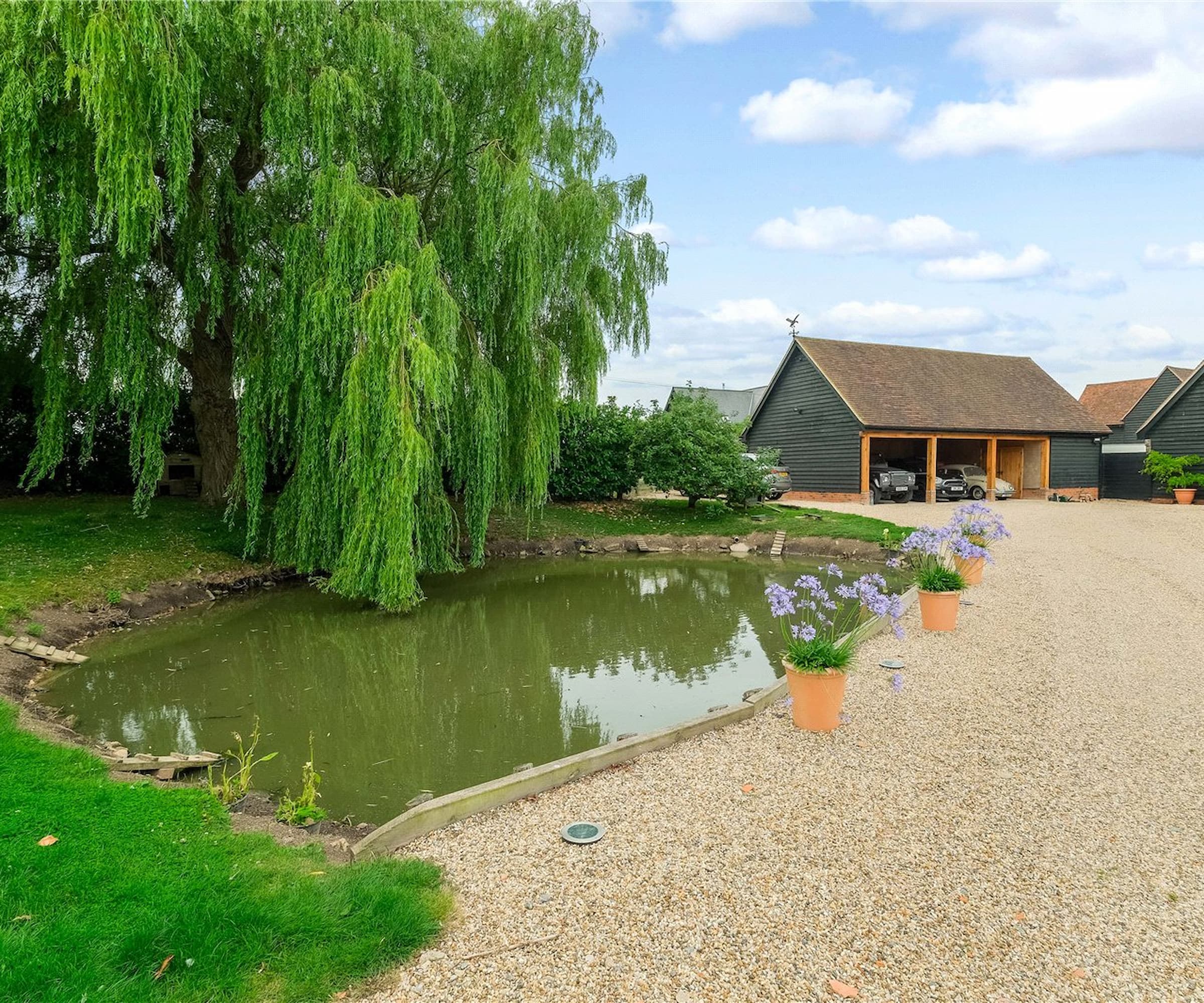 A garden pond with a willow tree overhanging next to a gravelled drive