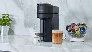 The Nespresso Vertuo Next on a countertop surrounded by coffe and Vertuo capsules