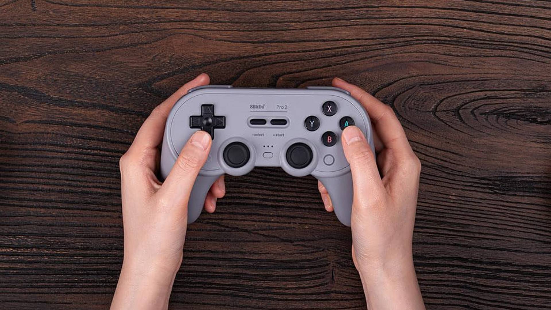 Hands holding 8Bitdo pro 2 over woodgrain table.