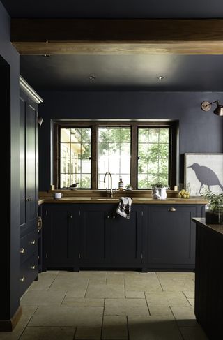black kitchen with black walls and units, stone floor, artwork, wall light, wooden countertop