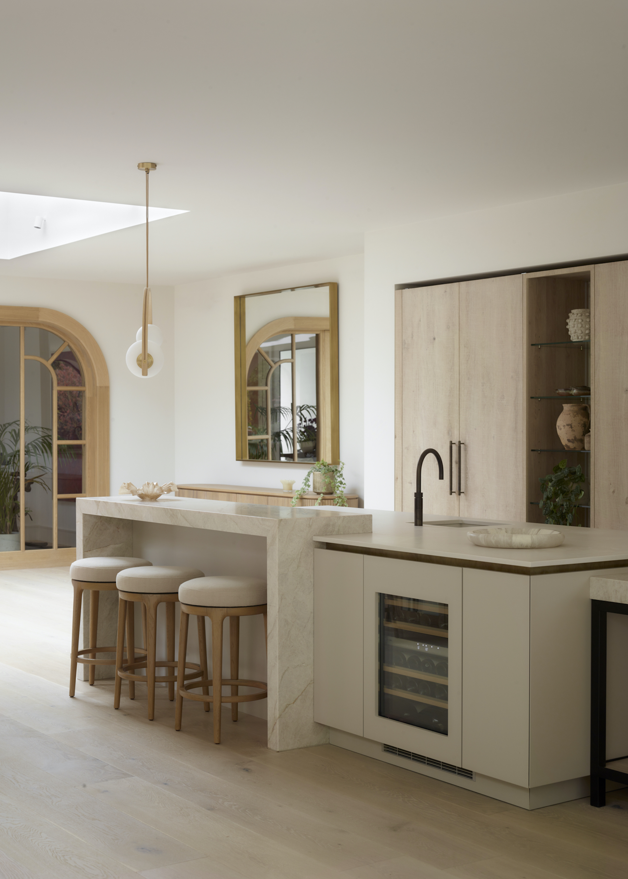 kitchen in pale beige and timber with an island in the middle that also has a wine fridge installed inside it