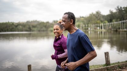 A happily retired couple jog side by side along a waterfront.