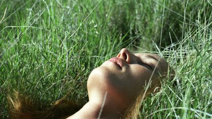 A woman lying in the grass trying the viral 5-4-3-2-1 grounding technique