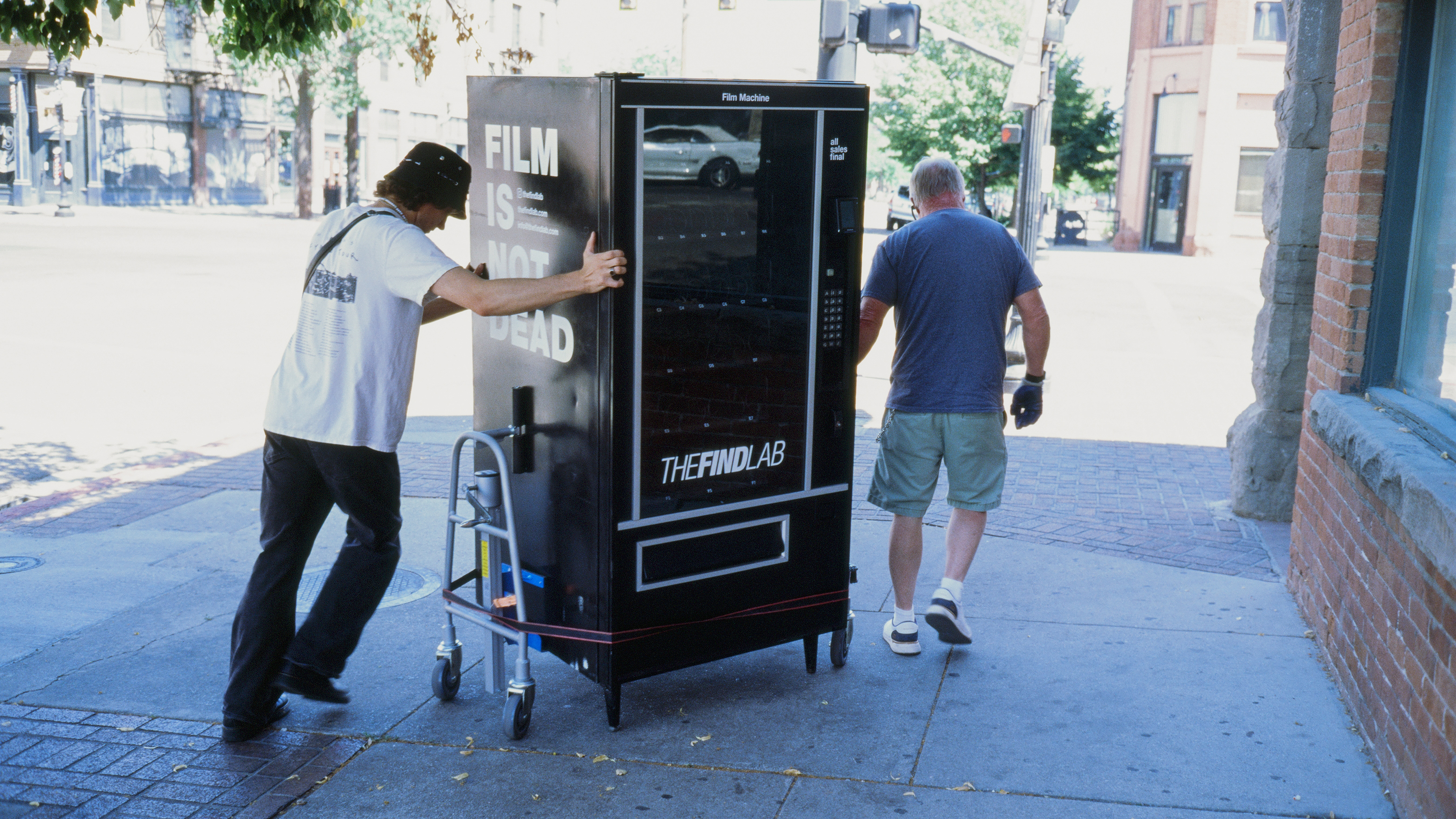 Two workers deliver a film vending machine to a pizza shop