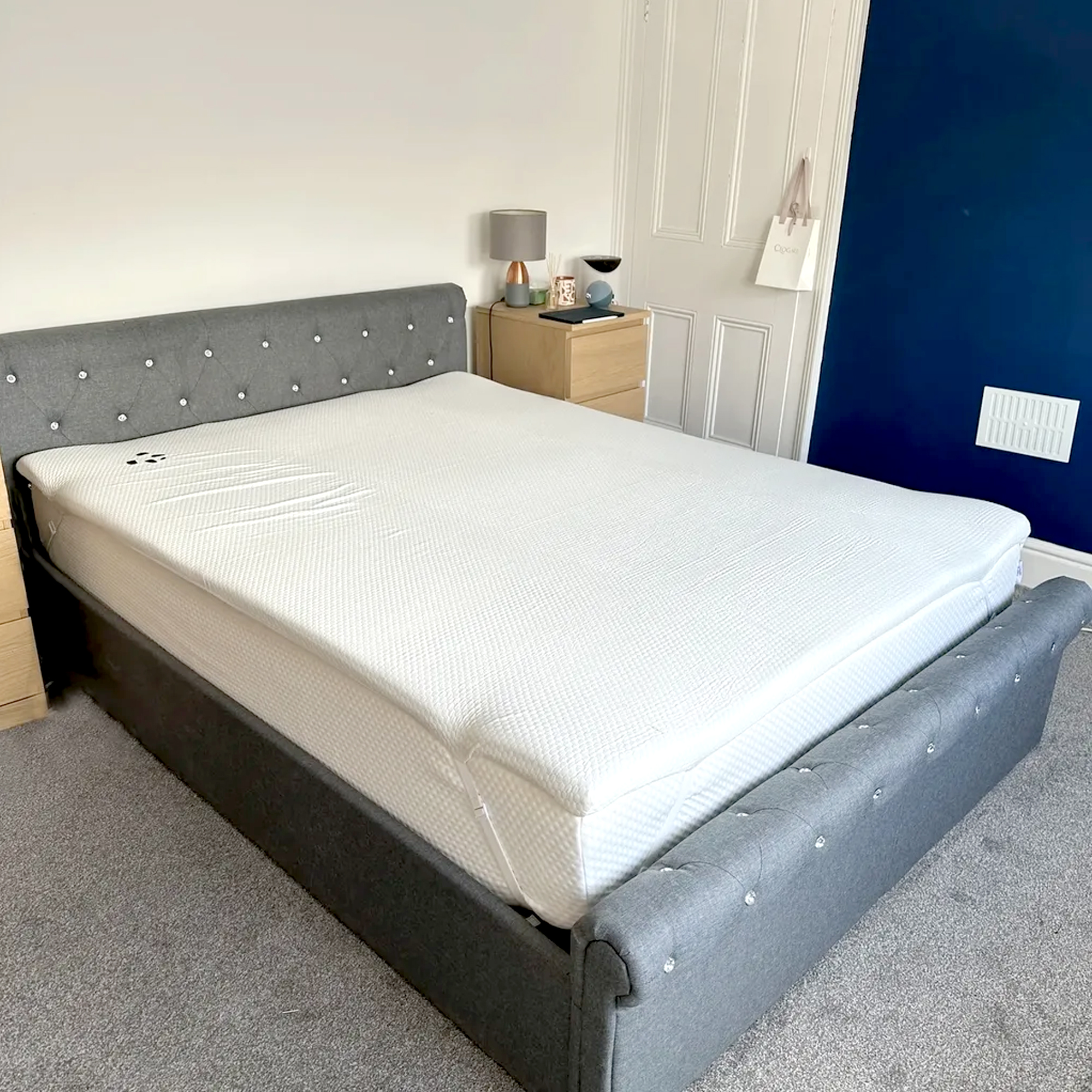 The Panda Topper being tested on top of a mattress on a grey upholstered bed in a bedroom