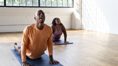 Two people in bright workout gear doing yoga in well-lit studio