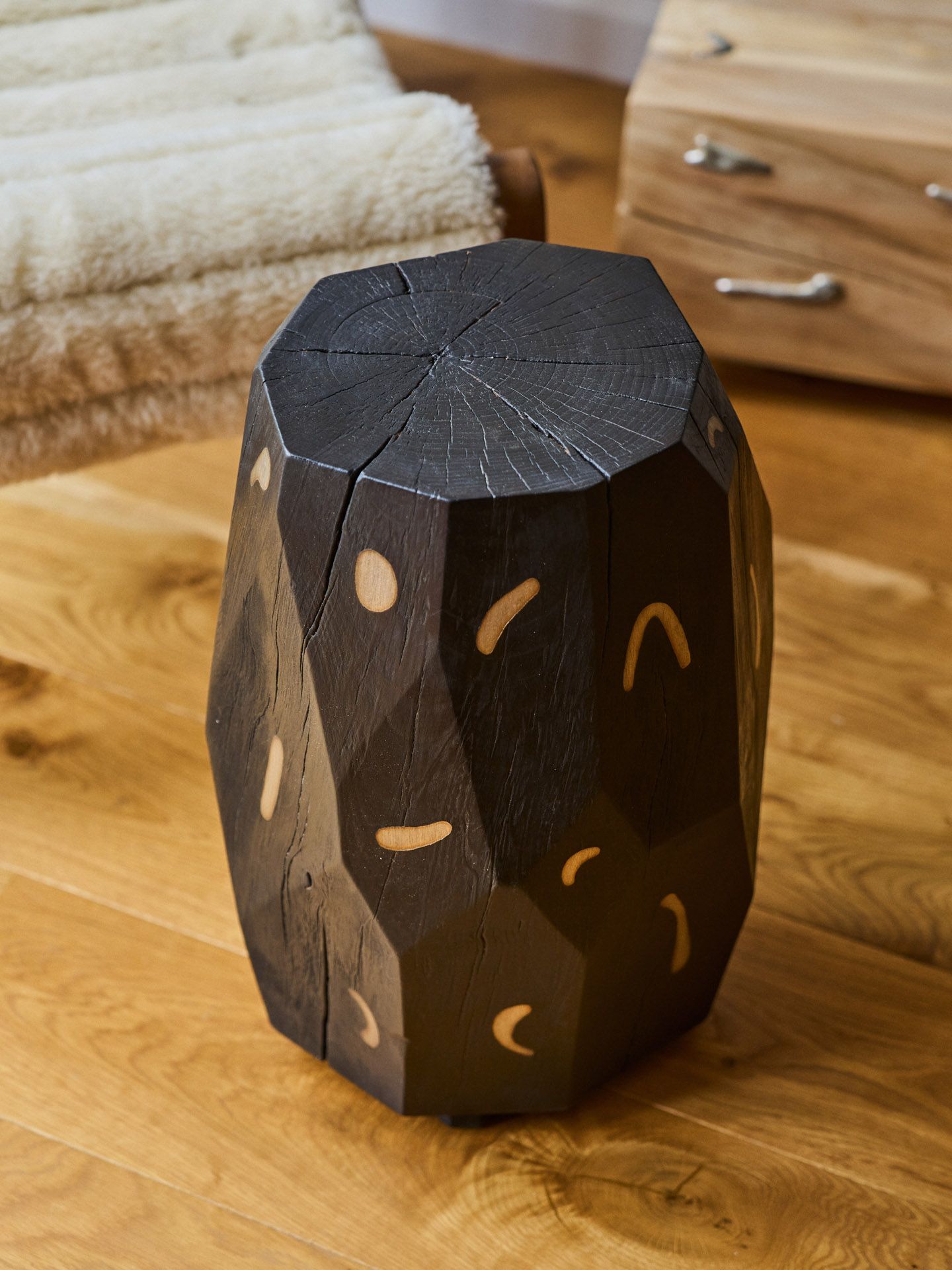 A stool cast from dark wood, decorated with golden abstract forms.