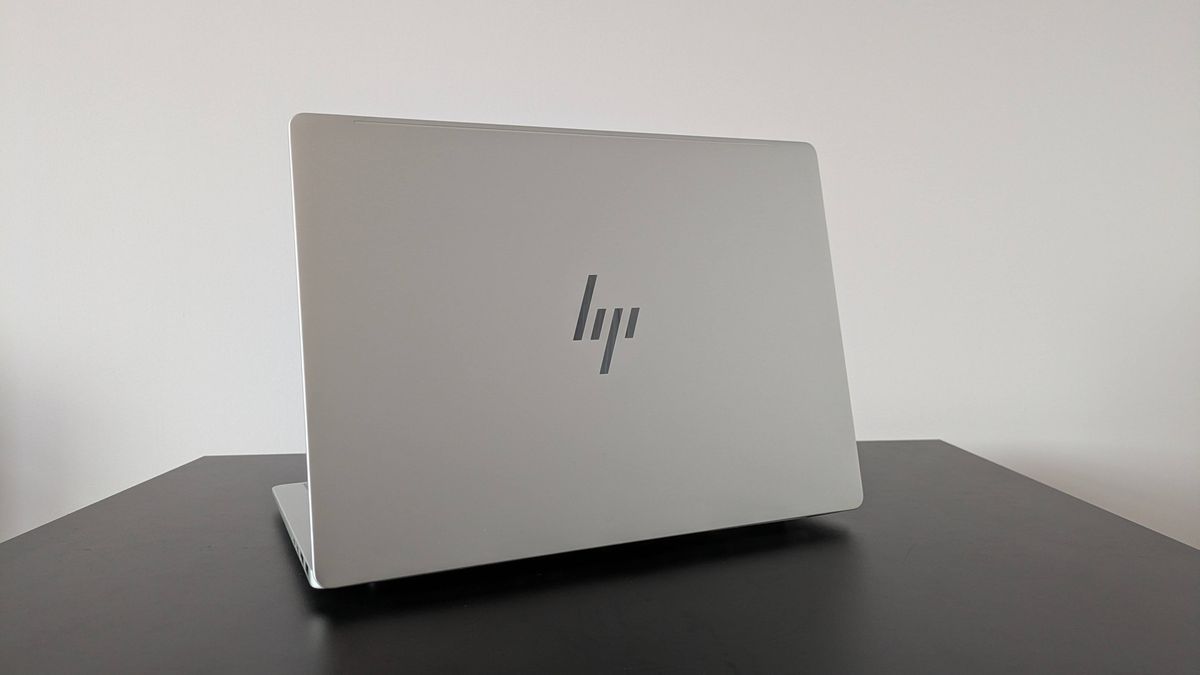 Rear three-quarter view of HP OmniBook 7 14-inch open on black desk with white wall in background