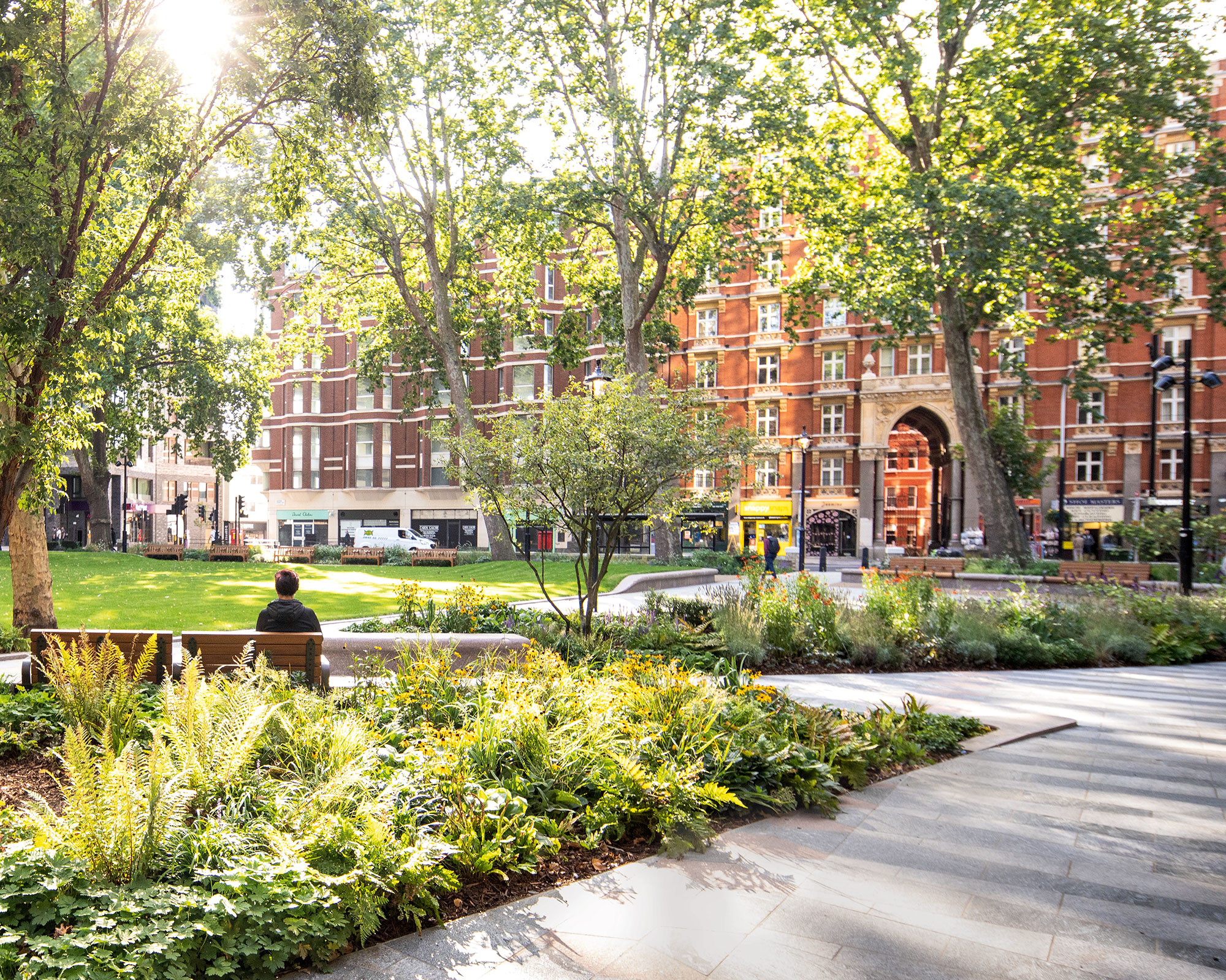 open-plan park area with green planting, bench seating, stone pavement