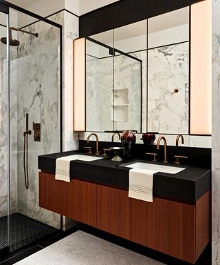 A bathroom with dark wood and black vanity, his and hers sinks and mirrors and a walks in shower