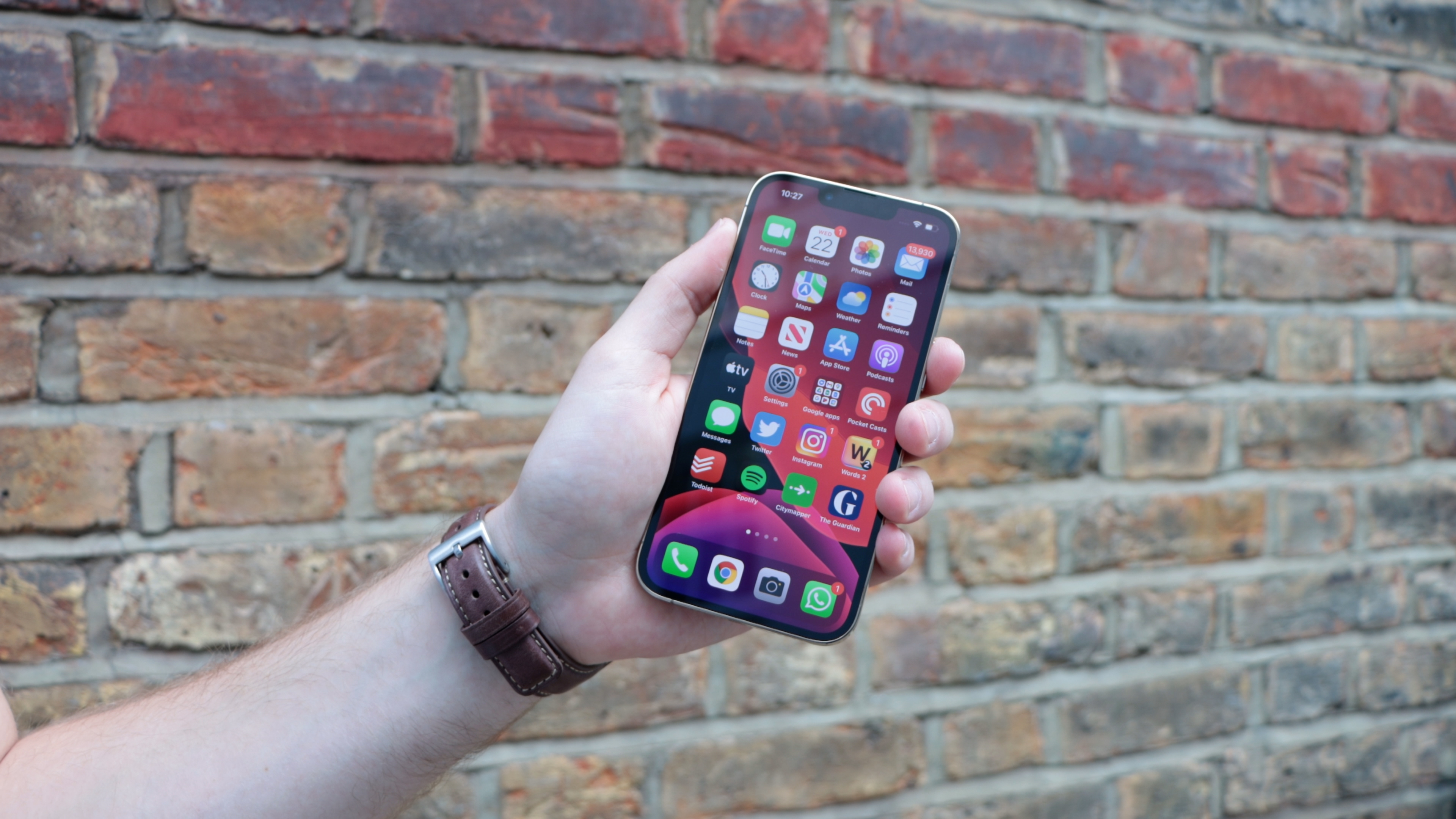An iPhone 13 Pro in someone's hand, with a brick wall in the background