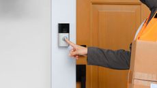 Someone delivering post and ringing a Ring doorbell on a white wall with a wooden front door