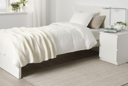 A neutral bedroom with a double bed , white sheets, and a neutral rug speckled with black threads on the floor