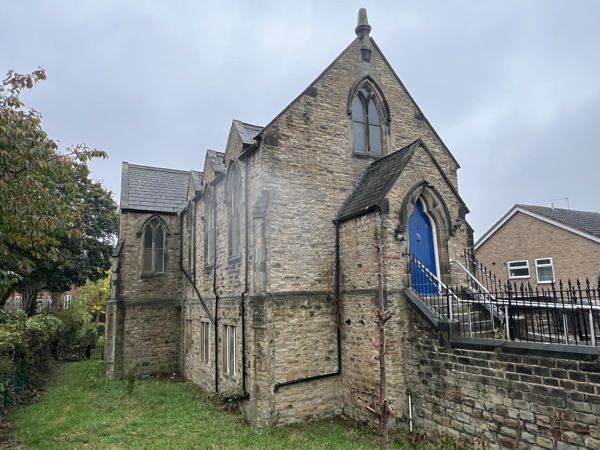 A stone church with gated walkway to the front door and surrounding garden lawn