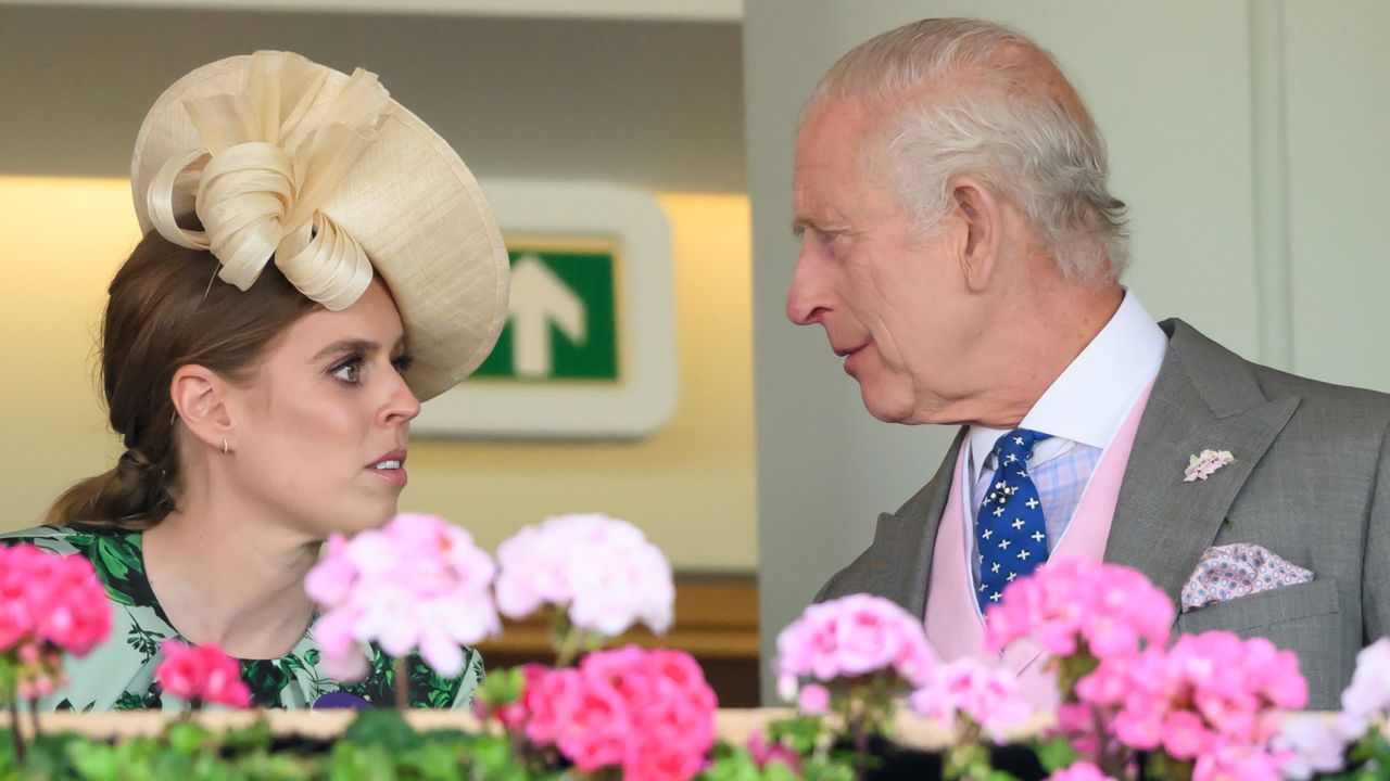 Princess Beatrice wearing a straw hat and green dress speaking with King Charles in a gray suit at Royal Ascot with pink flowers in the foreground