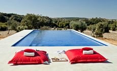 Pool area in nature with two red continental pillows with folded towels on top and a picnic platter for two between the pillows