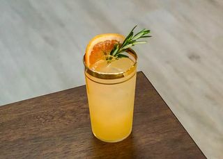 a tumbler filled with yellow cocktail. garnished with a grapefruit half-moon and a rosemary sprig